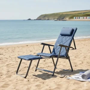 A portable camping chair with footrest positioned on a sandy UK beach, ideal for coastal holidays and staycations.