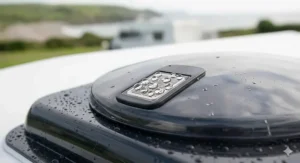 Close-up macro photograph focusing on the integrated rain sensor mechanism of the caravan roof vent fan, showing spherical water droplets on the metallic sensor grid.