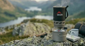 A side-by-side comparison of the three best backpacking stoves showing their weight in grams on a digital scale.