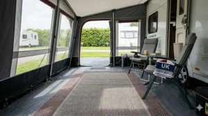 A high-quality 4K interior photograph of a full-sized caravan awning attached to a white caravan, showing a heavy-duty grey-charcoal durable groundsheet covered partially by a grey and burgundy patterned outdoor rug.