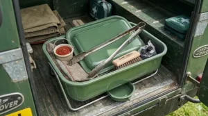 The internal storage of a small portable bbq containing metal tongs, a cleaning brush, and a small pot of tomato relish.