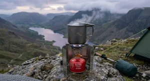 An ultralight titanium backpacking stove actively boiling water for wild camping at dusk on a remote mountain ridge in the Scottish Highlands, next to a tent.