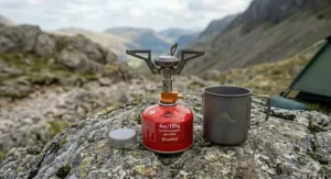 A detailed close-up showing an ultralight titanium backpacking stove next to a 100g MSR gas canister on a rocky outcrop in the Lake District.