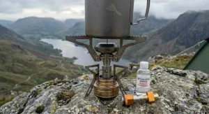 A detailed close-up showing the stability of an ultralight spirit burner stove's serrated pot supports holding a titanium mug on a rocky ridge in the Lake District.