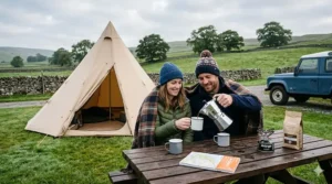 A classic stainless steel camping espresso maker heating up on a portable gas camping stove during a morning campout.