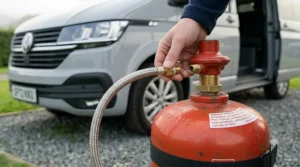 A hand connecting a braided gas hose to a regulator for a secure camping setup.