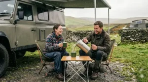 A couple enjoying fresh coffee made with a portable French press while sitting outside their motorhome on a rainy morning.