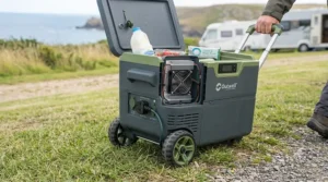 A portable electric cool box with ergonomic handle and wheels being pulled across grass.
