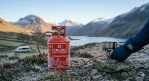 A person using a portable camping stove with a propane gas bottle in cold, frosty conditions.