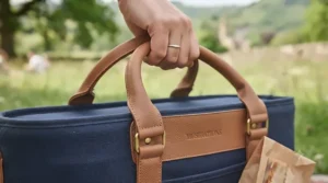 Close-up of a hand holding the comfortable leather carry handle of a cool bag.