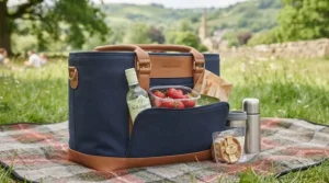 Close-up of a navy blue cool bag with tan leather trim on a tartan blanket.