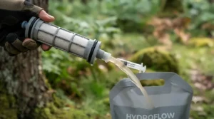Backwashing the gravity water filter element to maintain flow rate during extended group expeditions.