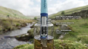 A runner using a squeeze-style portable water filter to drink fresh water straight from a natural water source on a trail.