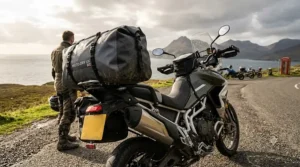 Black waterproof dry bag strapped to the rear rack of an adventure motorcycle on a wet UK road.