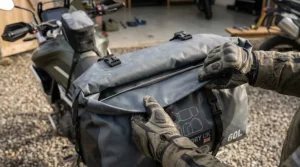 Hands rolling down the waterproof closure of a heavy-duty motorcycle dry bag.